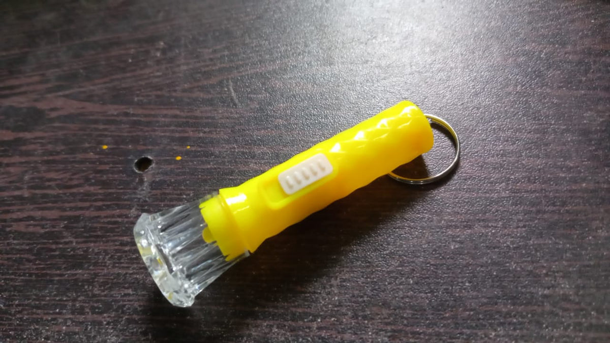 A yellow plastic flashlight with a clear faceted head and a silver keyring is on a dark brown wooden surface.