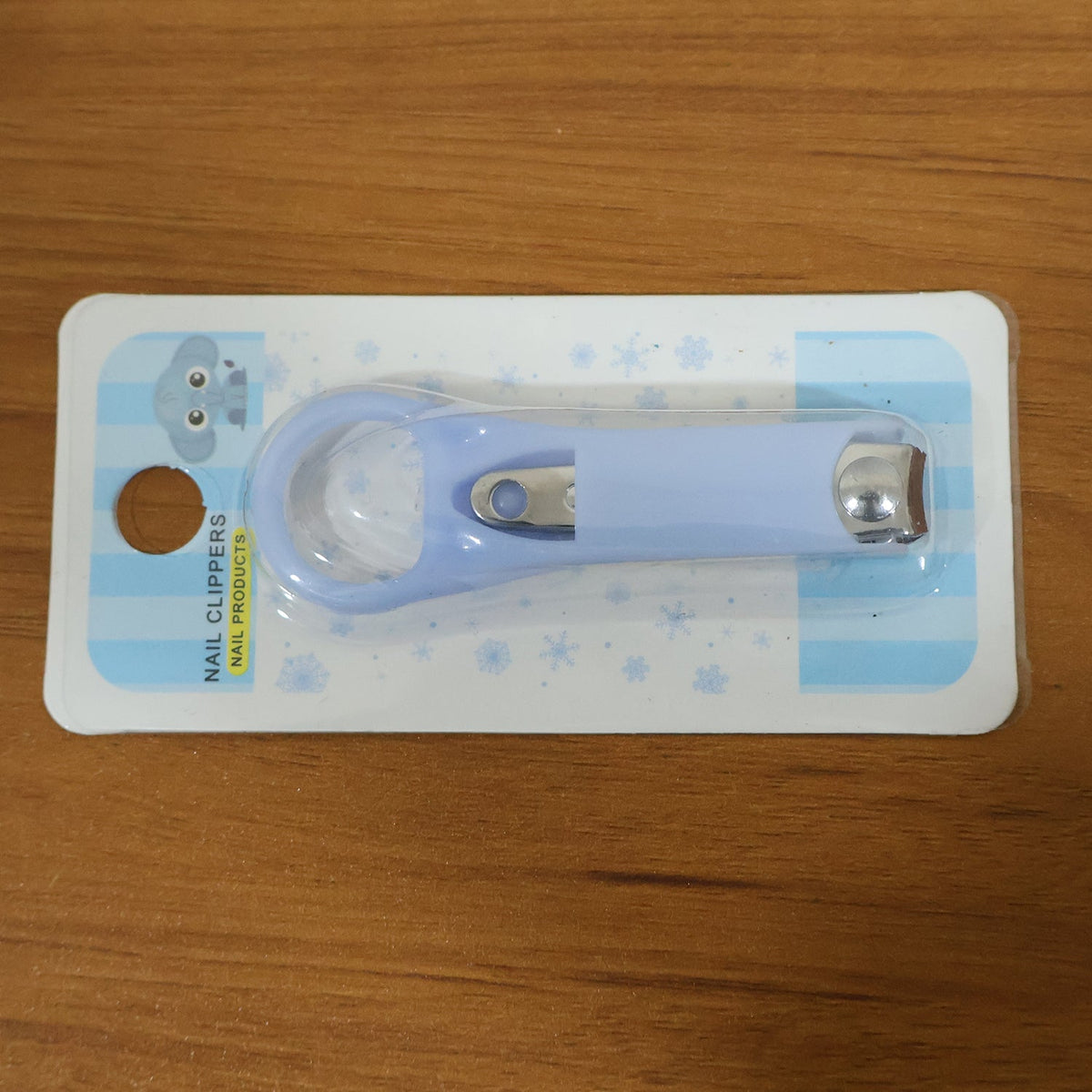 A light blue baby nail clipper in clear plastic packaging with blue and white striped backing on a wooden surface.