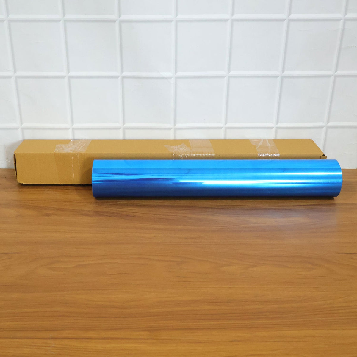 A rolled blue mirror film and a brown cardboard box on a wooden surface.