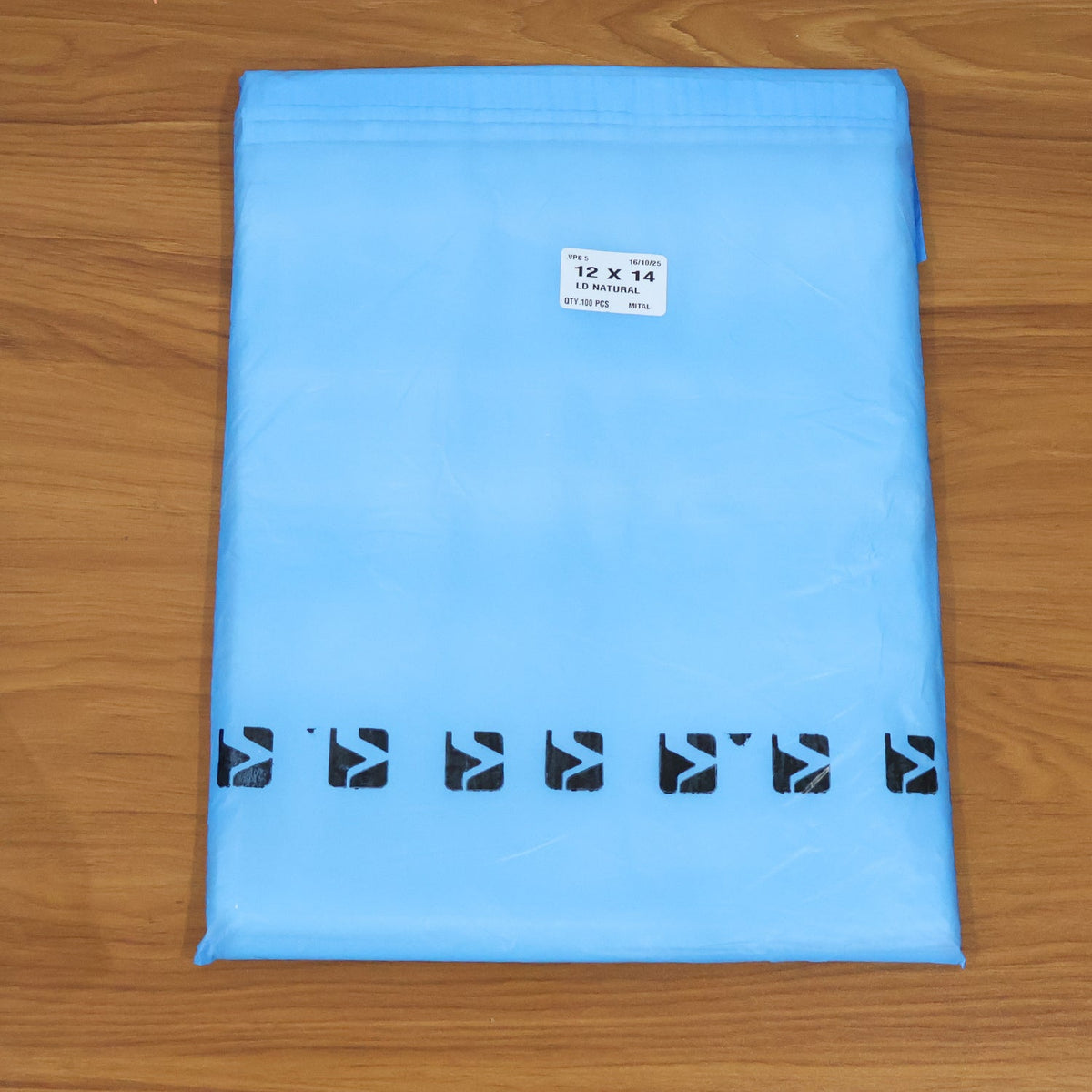 A light blue polybag with black arrow designs and a white label, on a wooden surface.