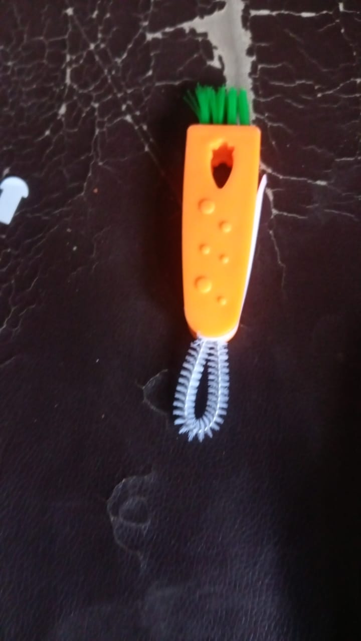 The orange 3-in-1 cleaning brush with green bristles and a white crevice tool lies on a dark brown textured surface.