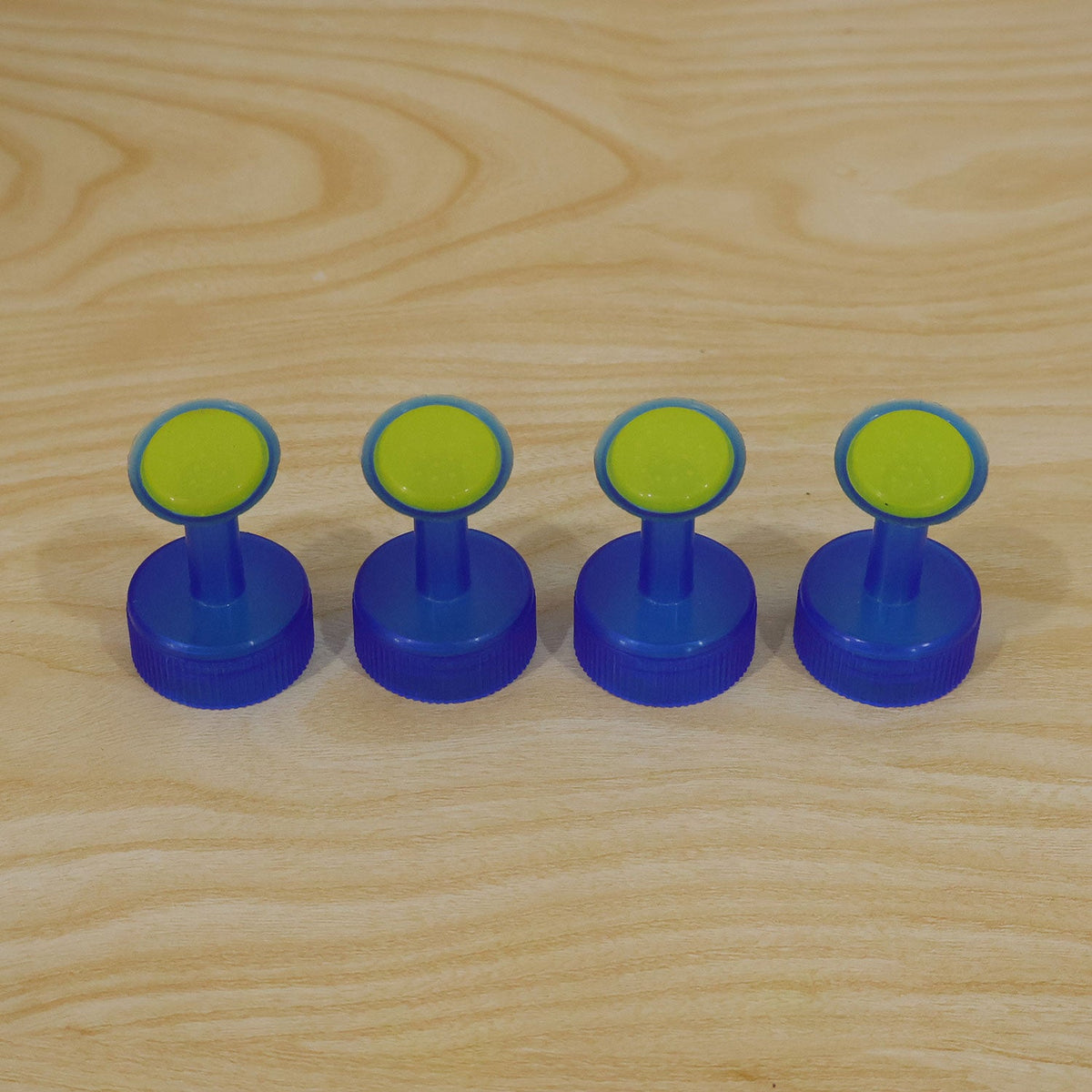 Four identical blue and green plastic bottle cap sprinklers are lined up neatly on a light wooden surface.