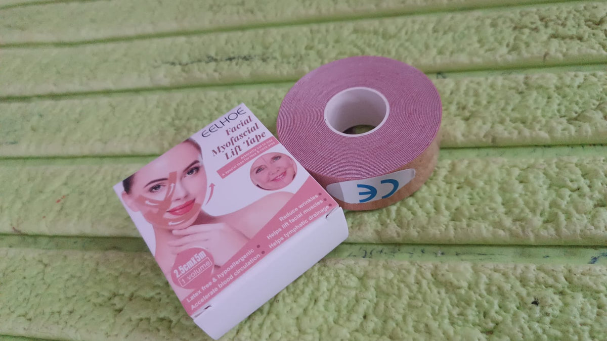 A pink roll of facial tape and its white product box resting on a textured green towel.