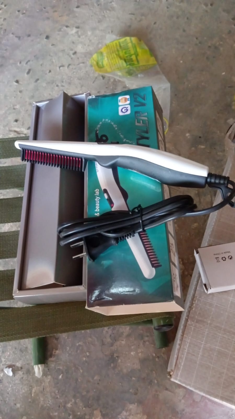 A white and black electric hair and beard straightening comb with its cord is shown next to its product box on a textured