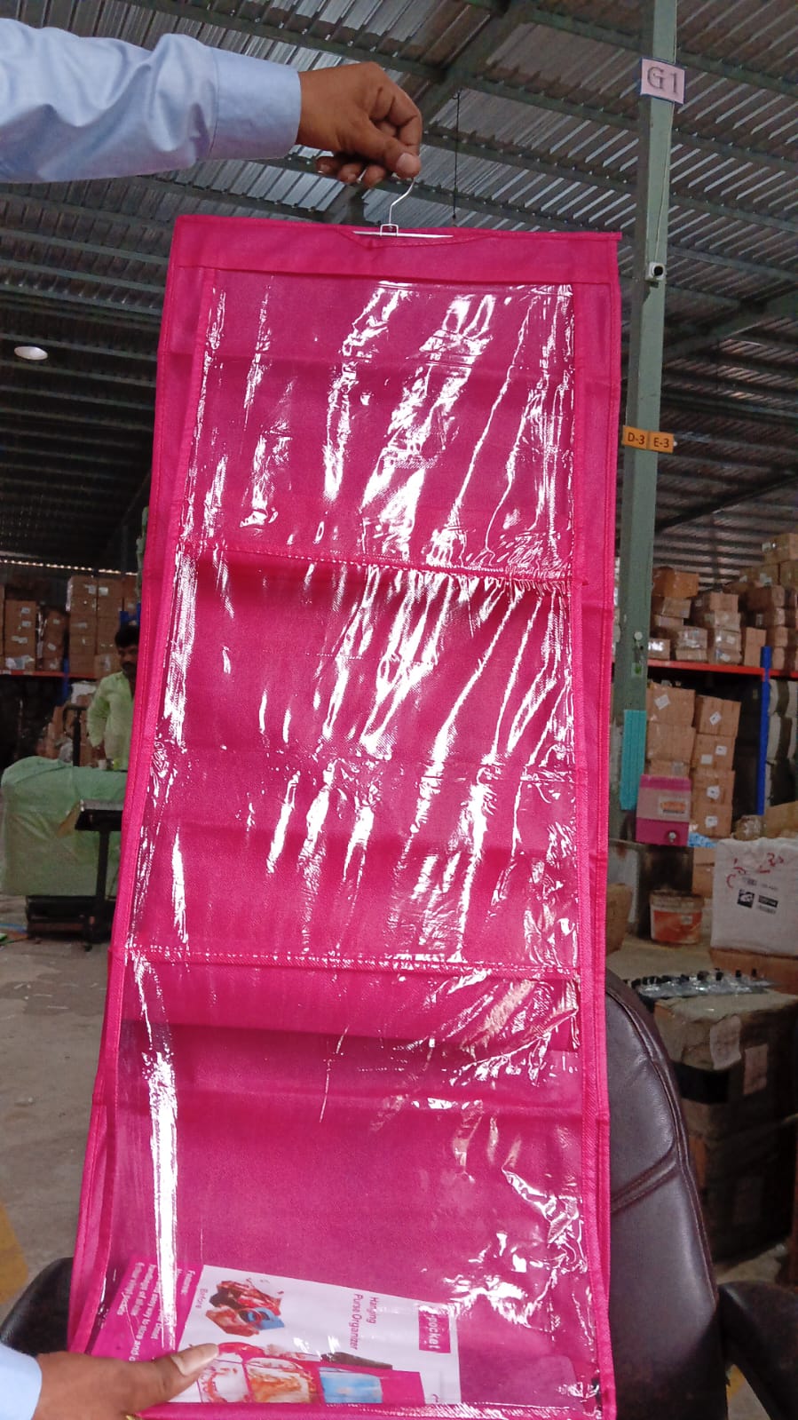 A person holds up a pink hanging purse organizer with clear pockets in a warehouse setting.