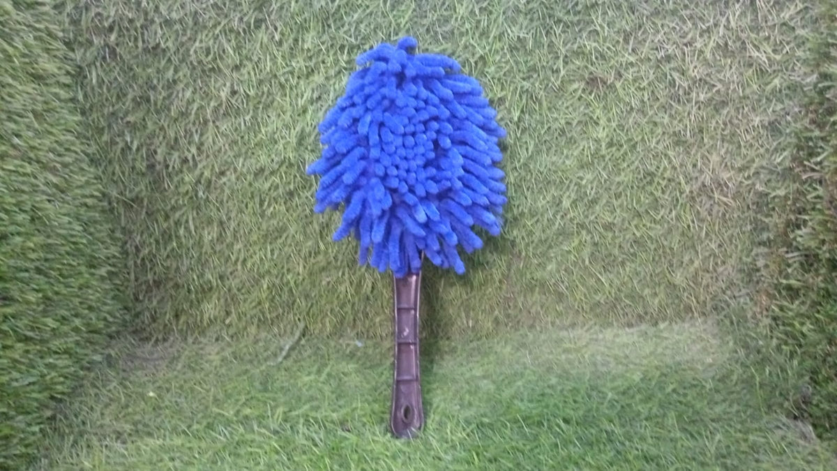 Blue microfiber duster with a black handle standing upright on a green artificial grass background.
