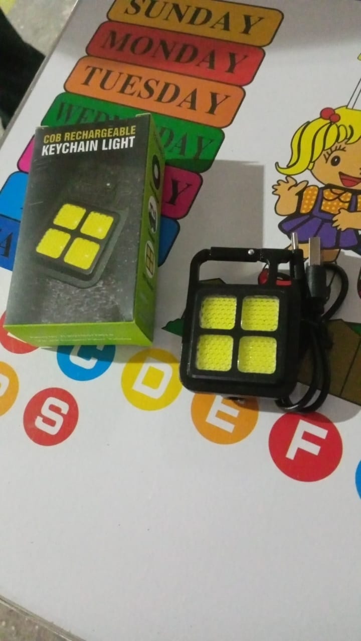 The black LED keychain light and its green packaging box resting on a colorful mat with letters and days of the week.