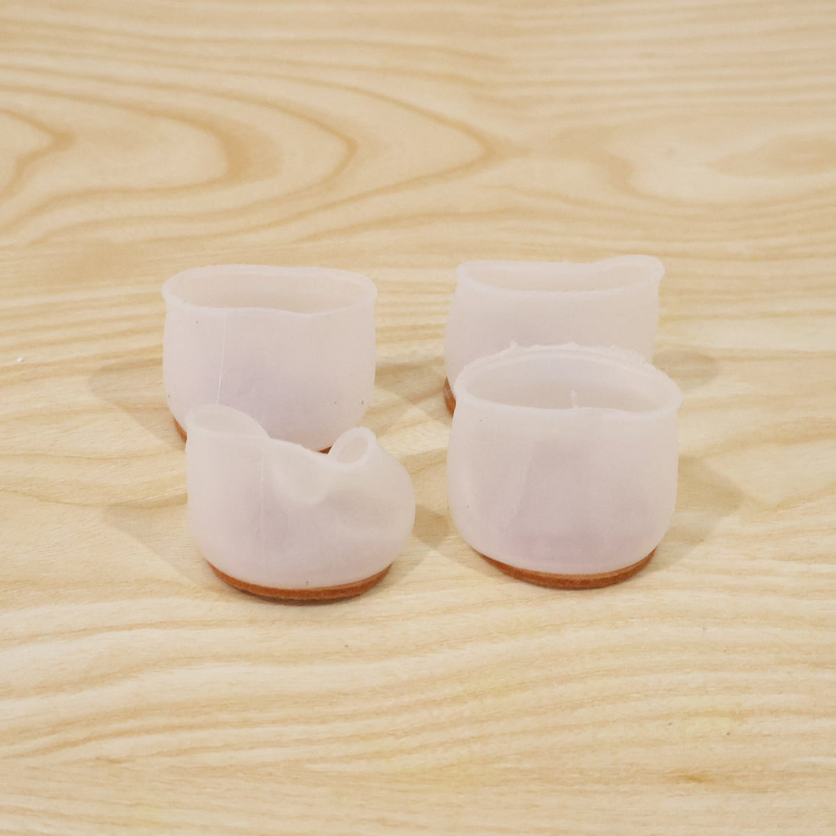 Four translucent silicone furniture leg protectors with felt bottoms on a light wooden surface.