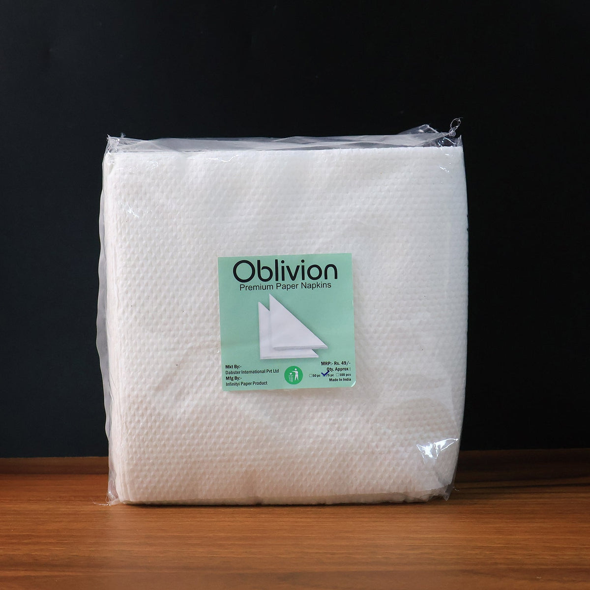 A clear plastic-wrapped package of Oblivion brand premium paper napkins on a wooden surface.
