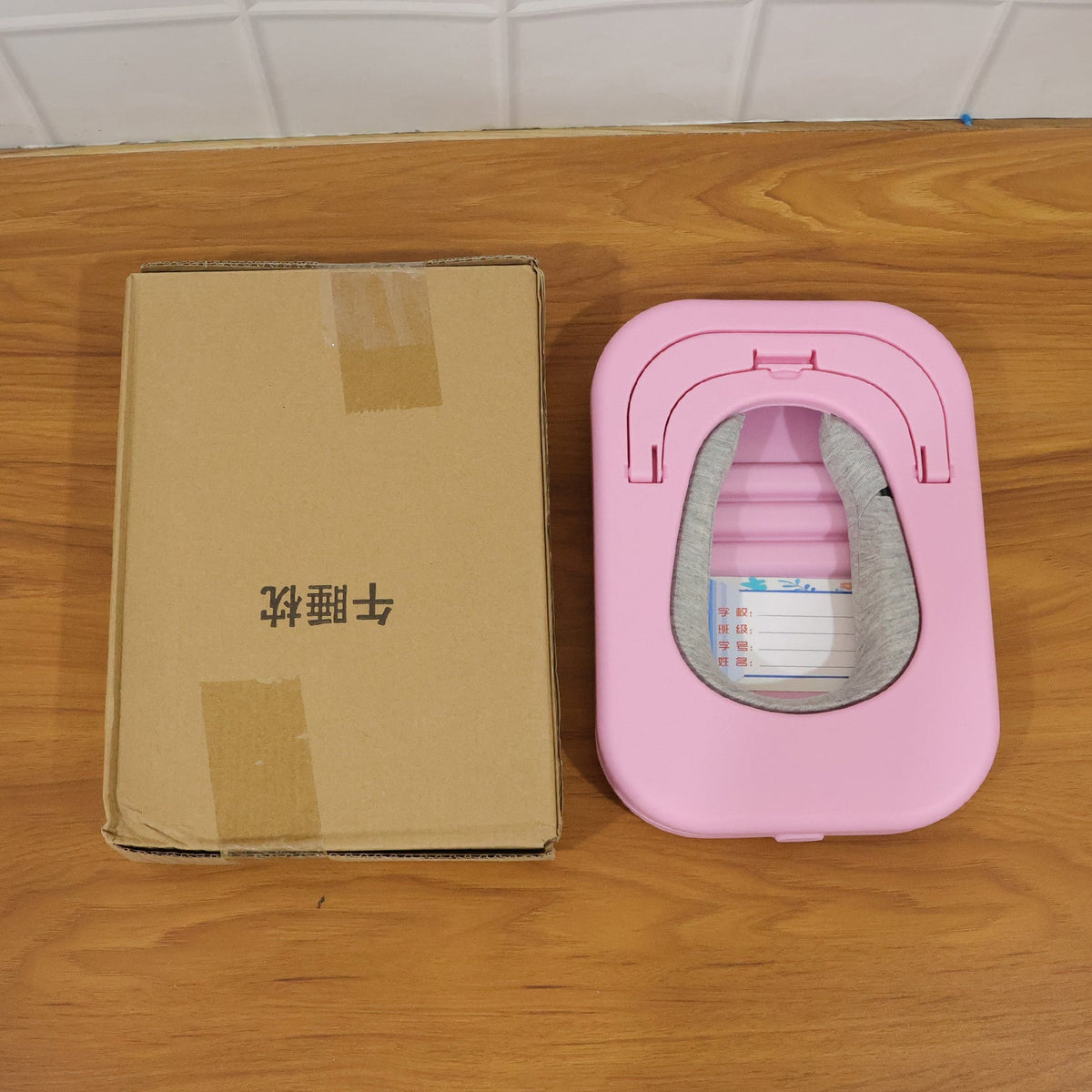 A brown cardboard box and the folded pink desktop nap pillow are placed side-by-side on a wooden surface.