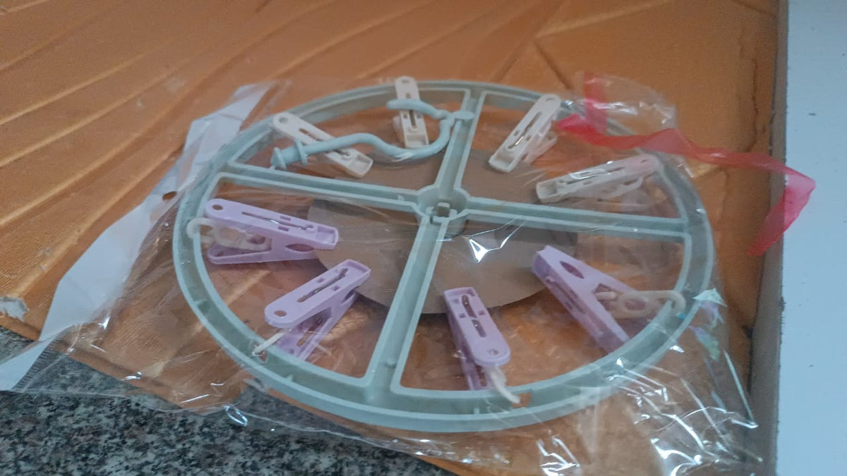 A light blue circular drying rack with purple and white clips is sealed in clear plastic packaging.