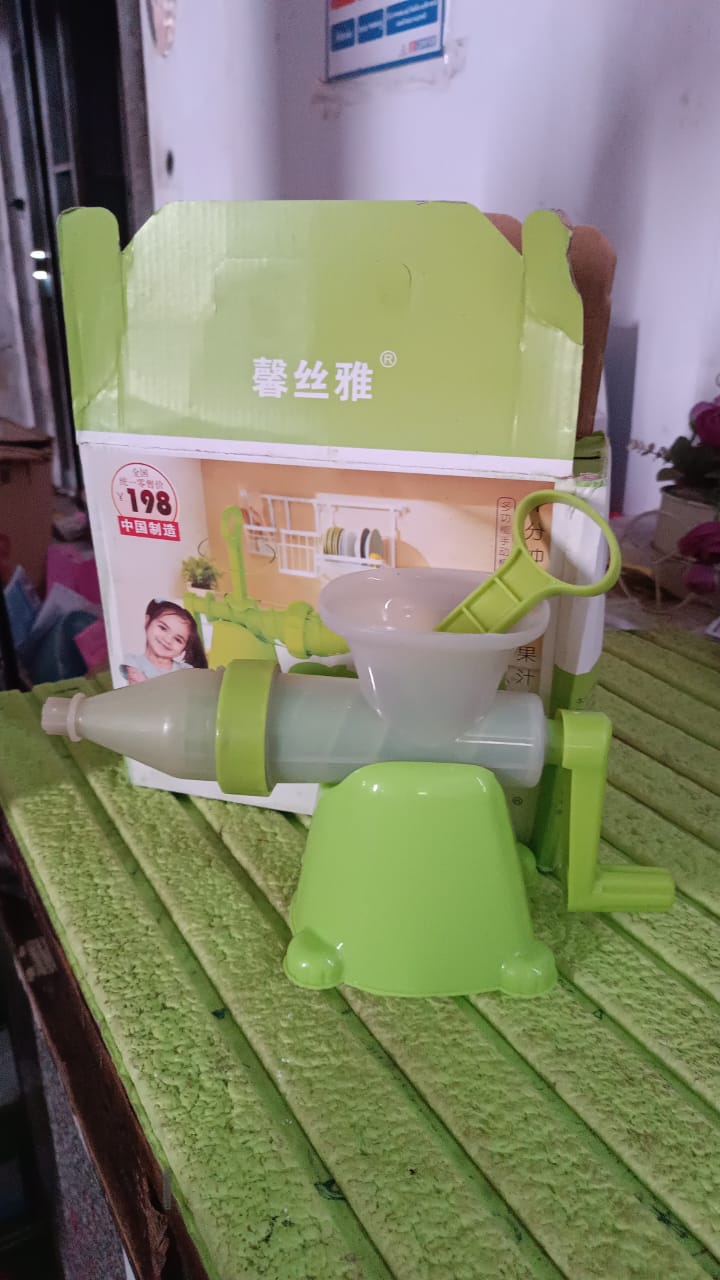 A green manual juicer and its components displayed in front of its product box on a textured green surface.
