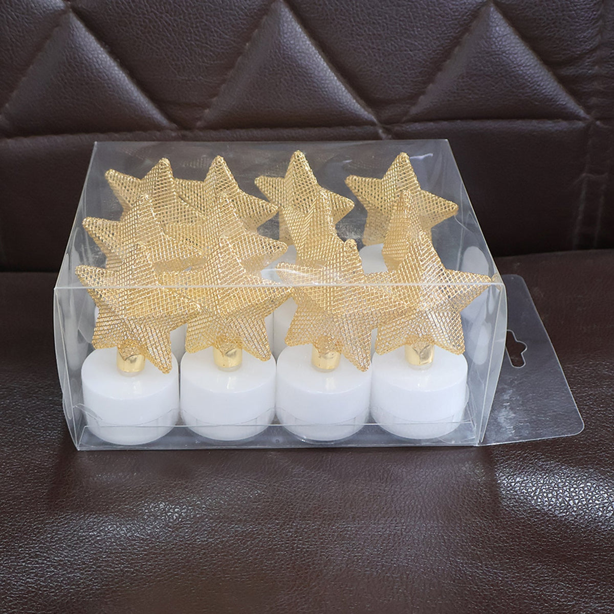 Twelve LED tealights with golden mesh stars packaged in a clear plastic box on a brown textured surface.