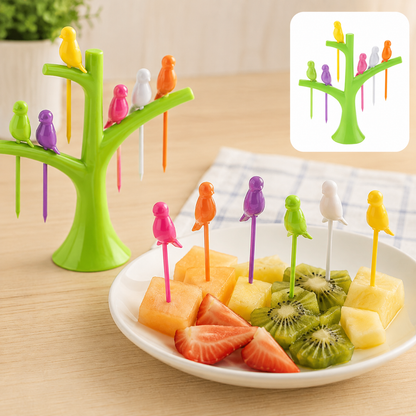 A green tree holder with colorful bird fruit forks in a plate of cut fruit, including kiwi, pineapple, and strawberries.