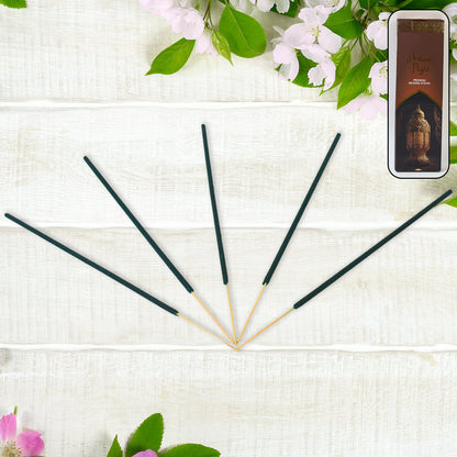 Five green incense sticks fanned out on a white wooden surface with a small brown box in the corner.