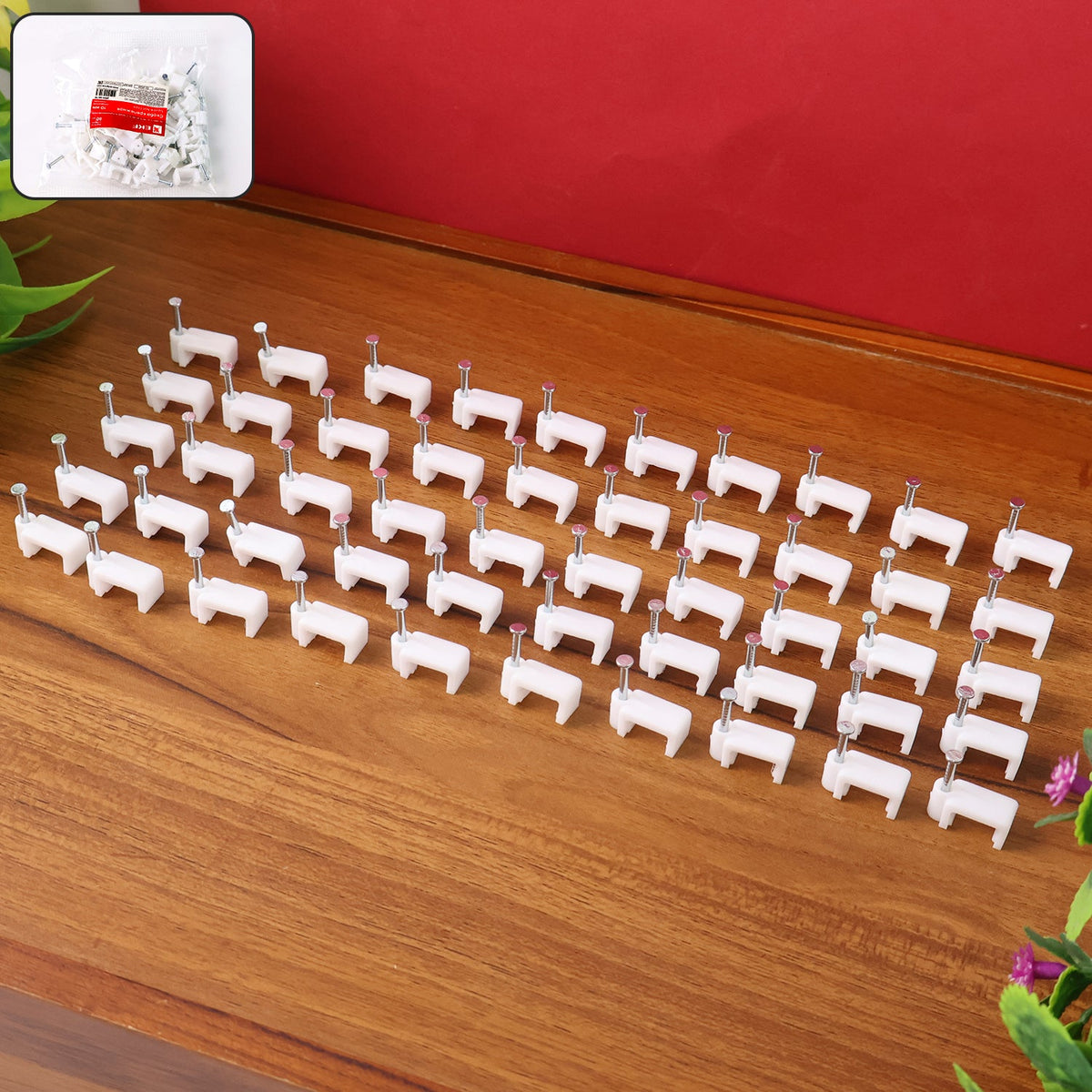 Fifty white plastic cable clips with nails laid out in organized rows on a wooden table, with a small bag of clips visible