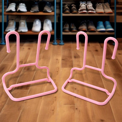 Two pink plastic shoe drying racks are on a wooden floor, with a blurred background of a shoe shelf.