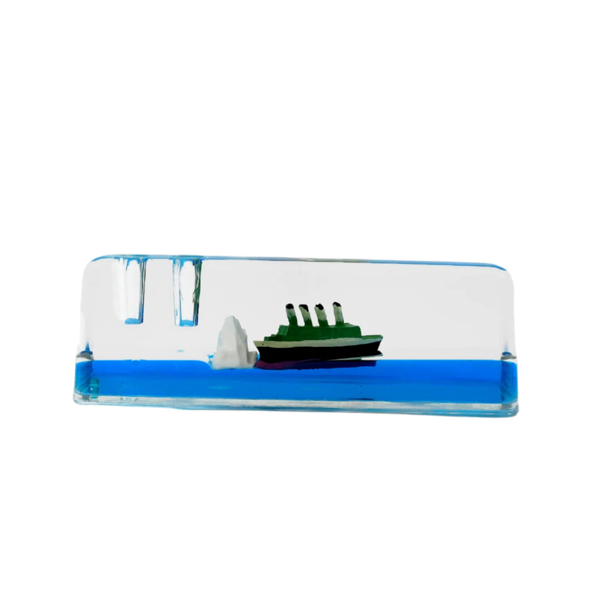 A clear rectangular liquid motion paperweight with a green ship and iceberg floats in blue liquid on a plain white