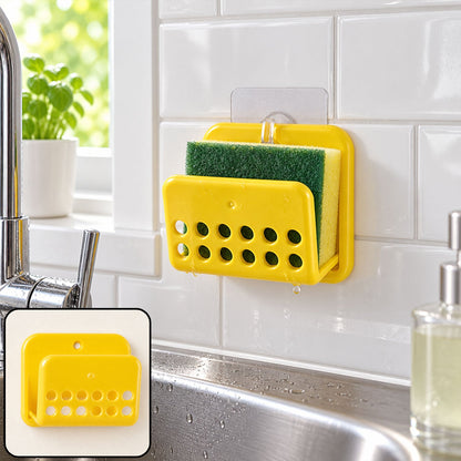 A yellow plastic sponge holder with a green sponge, adhered to white tiled kitchen wall above a sink. Small inset shows