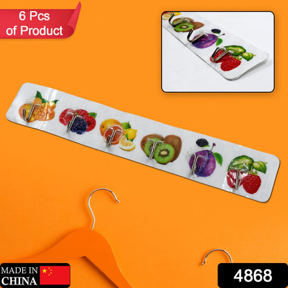 A white adhesive wall hook strip with fruit designs is displayed against a vibrant orange background with a hanger.