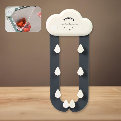 A white cloud-shaped holder with dark grey rain-like arms and white raindrop hooks against a brown and wooden background.