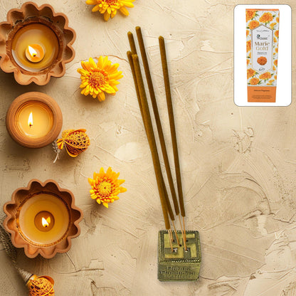 Four brown incense sticks in a gold holder, surrounded by yellow marigolds and three lit diyas.