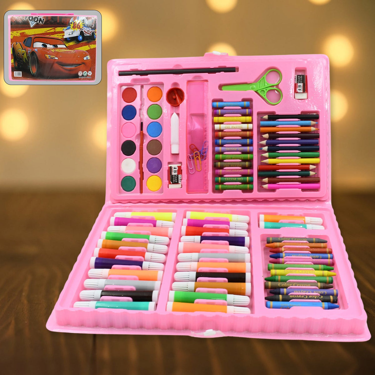 An open pink art kit with various drawing tools sits on a dark wooden surface, with a Cars movie image in the corner.