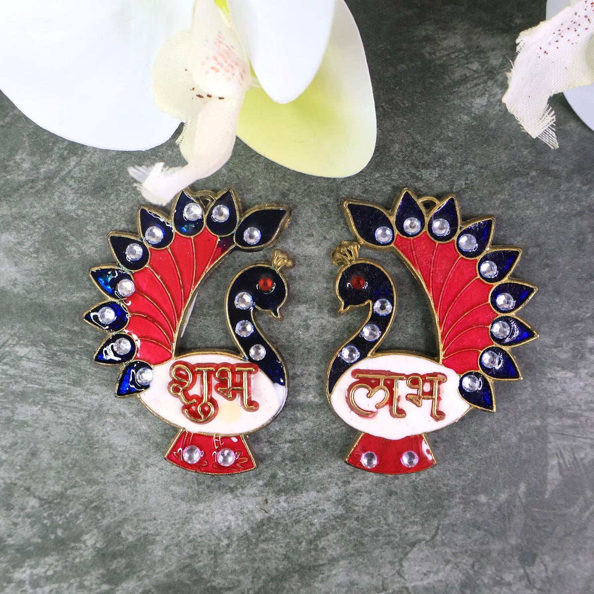 Two colorful peacock-shaped Shubh Labh wall hangings with red, blue, and white enamel, adorned with clear rhinestones on a