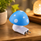 A blue and white mushroom-shaped night light with a two-pin plug sits on a wooden surface next to a plant.