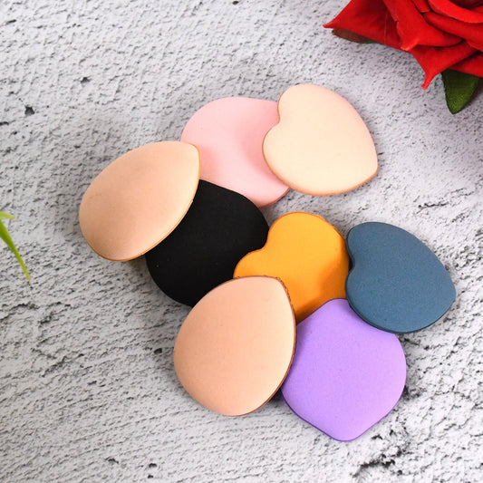 Eight colorful makeup sponges in various shapes and colors scattered on a textured gray surface.