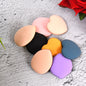 Eight colorful makeup sponges in various shapes and colors scattered on a textured gray surface.