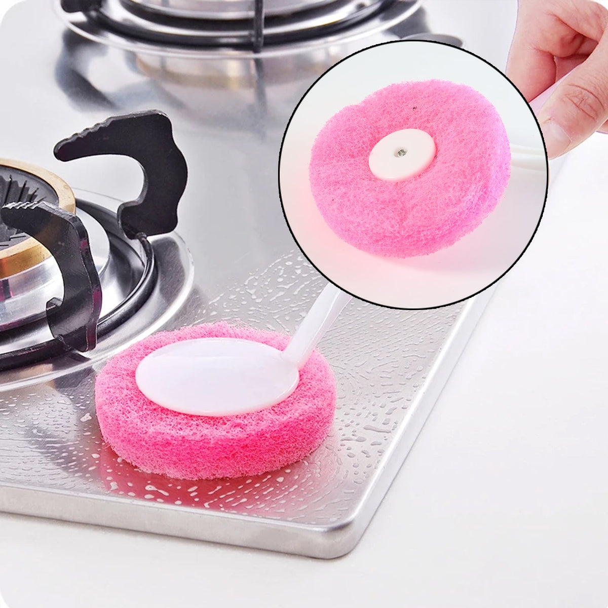 A pink and white scrubber cleans a stainless steel stovetop with soap suds next to a burner.
