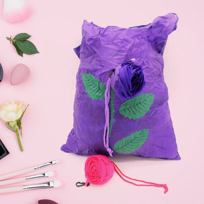 A purple foldable shopping bag with a rose design lies flat next to a pink folded bag on a pink surface.
