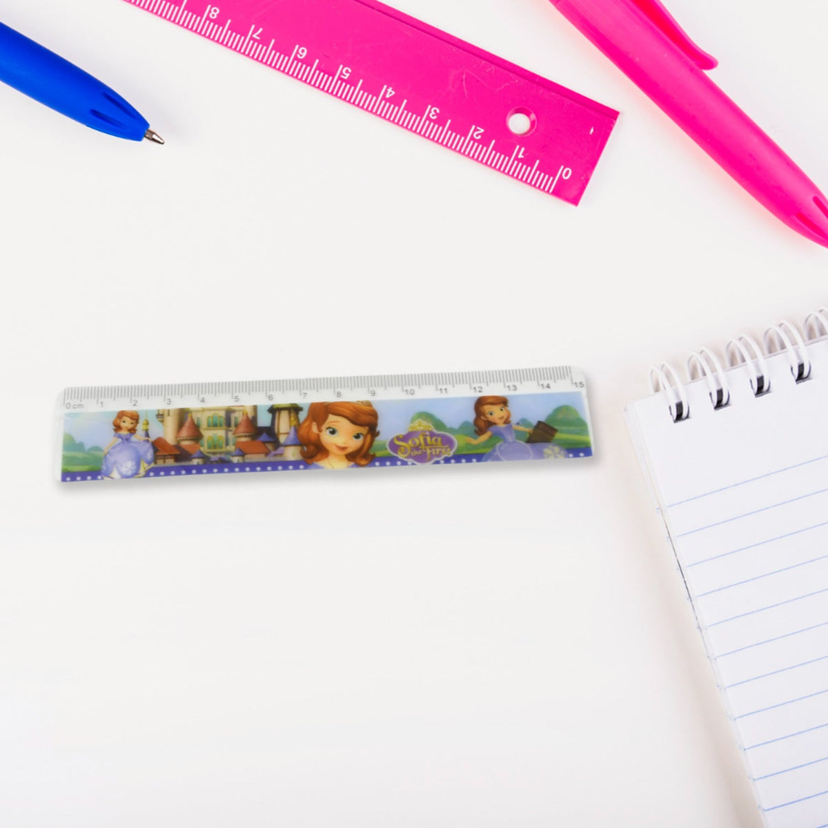A Sofia the First ruler on a white desk next to a spiral notebook, with a blue pen and pink ruler in the background.