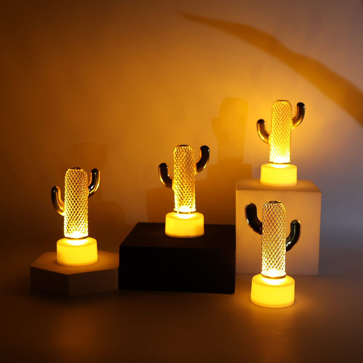 Four glowing cactus-shaped LED lights are arranged on various dark and light blocks, emitting a warm light.