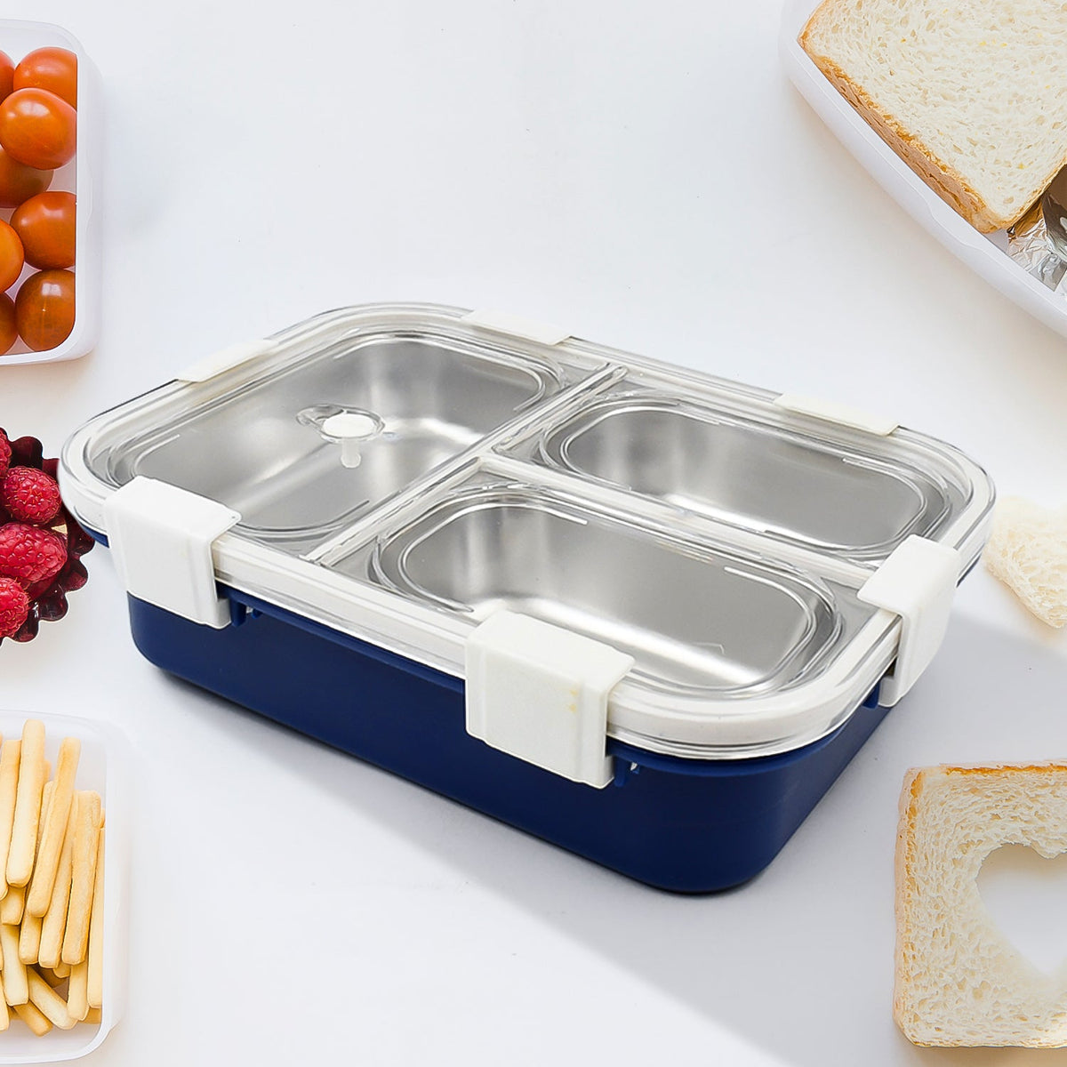 A blue lunch box with three stainless steel compartments, white clasps, and a silver spoon on a white background.