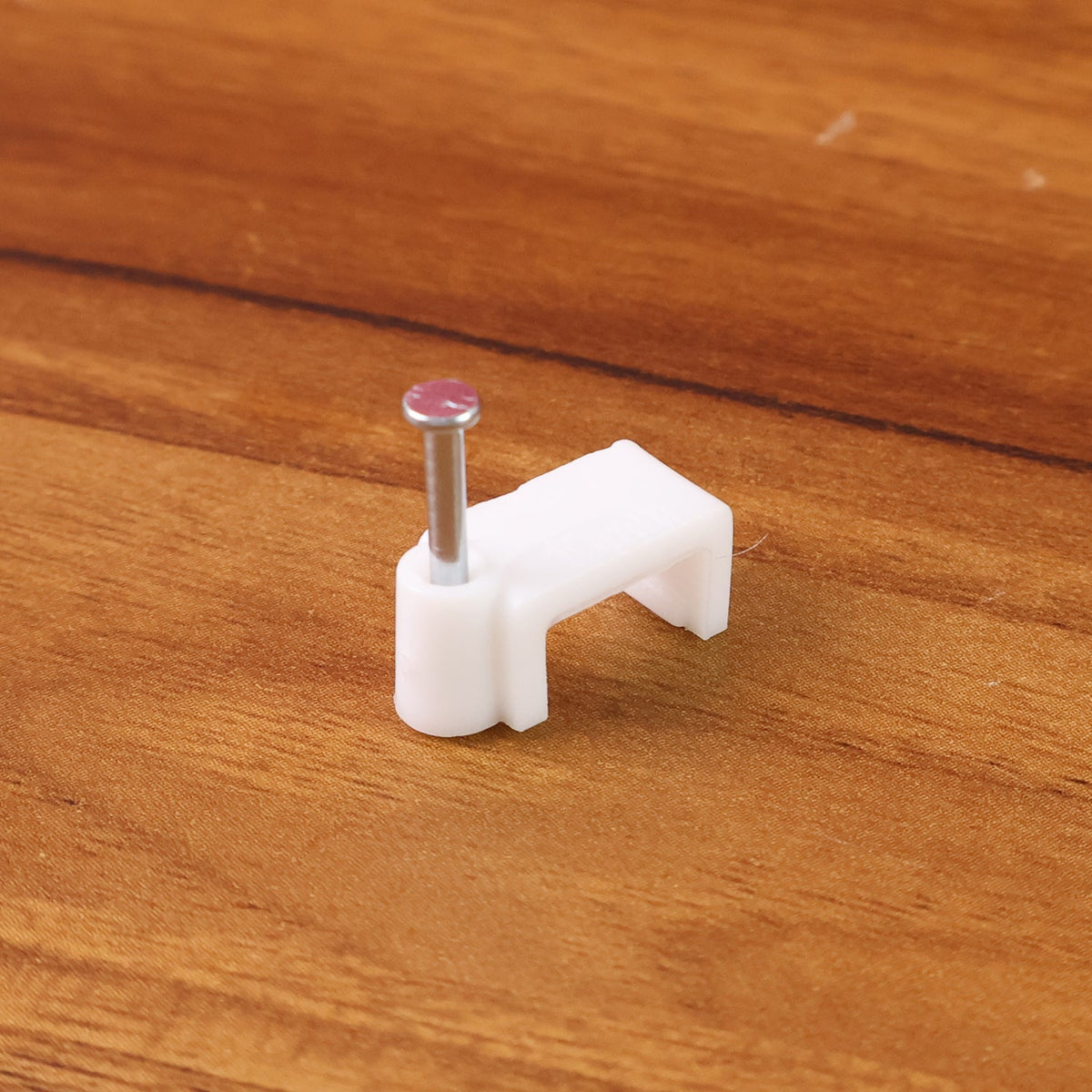 A single white plastic cable clip with a nail on a wooden surface.