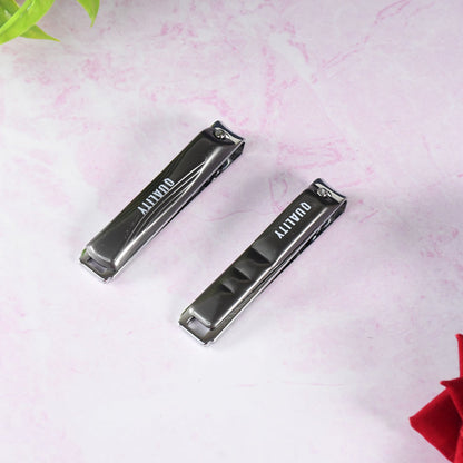 Two closed black and silver nail clippers with "QUALITY" on the handles, on a pink marble surface.