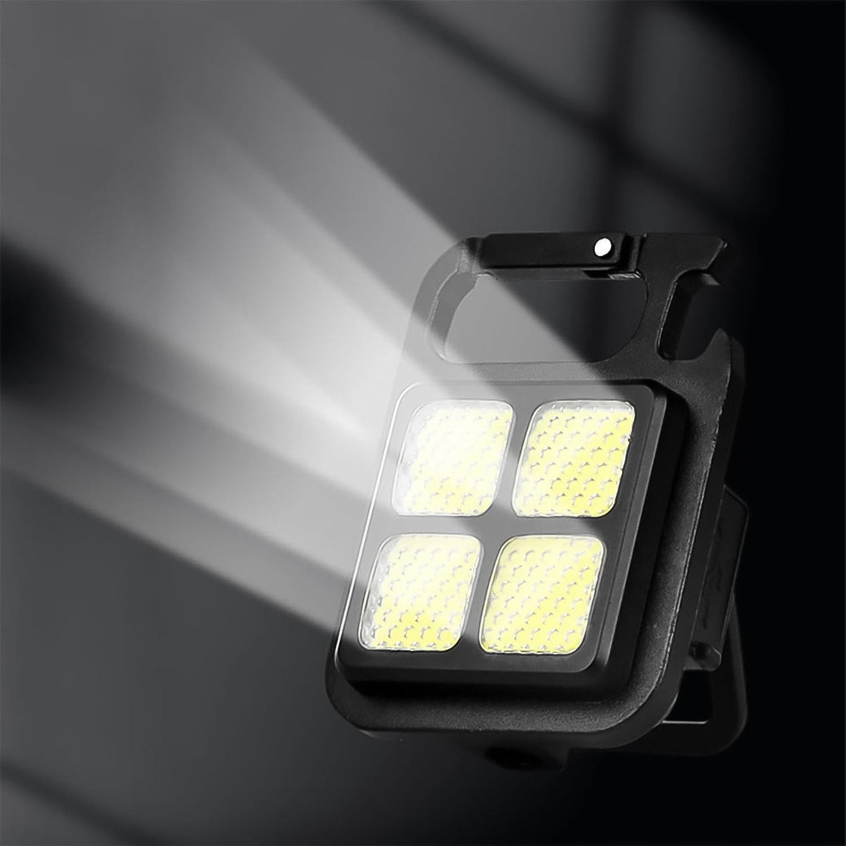 The black LED keychain light illuminated, casting a bright white beam of light to the left against a dark background.