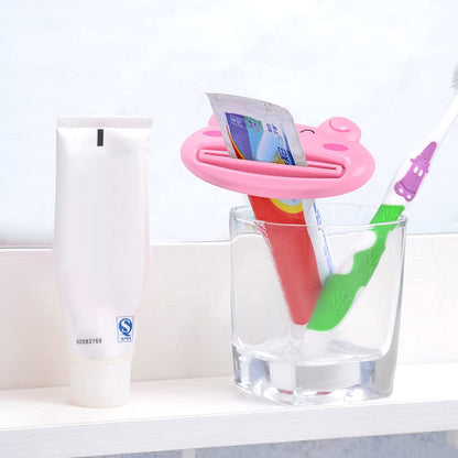 A pink pig-shaped toothpaste squeezer holding a red and white toothpaste tube upright in a clear glass next to a white tube