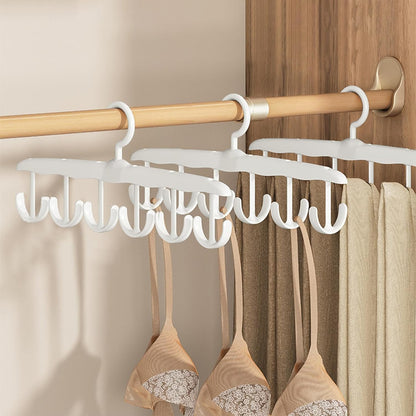 Three white plastic multi-hook hangers on a wooden rod, holding bras and pants in a closet.