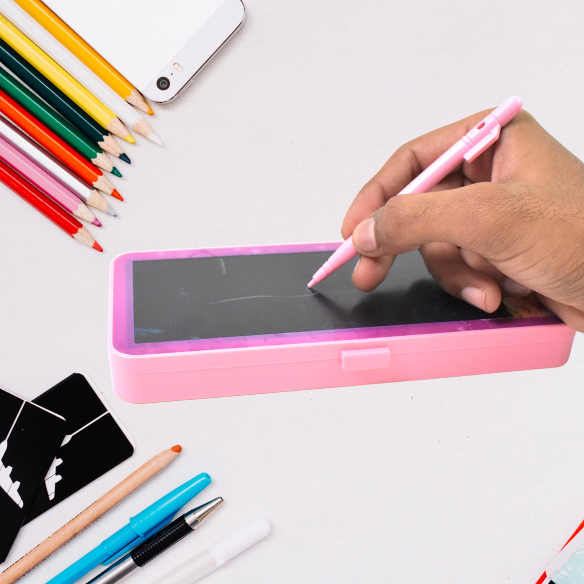 Pink LCD writing tablet pencil case with a hand holding a pink stylus, drawing on the black screen, surrounded by stationery.