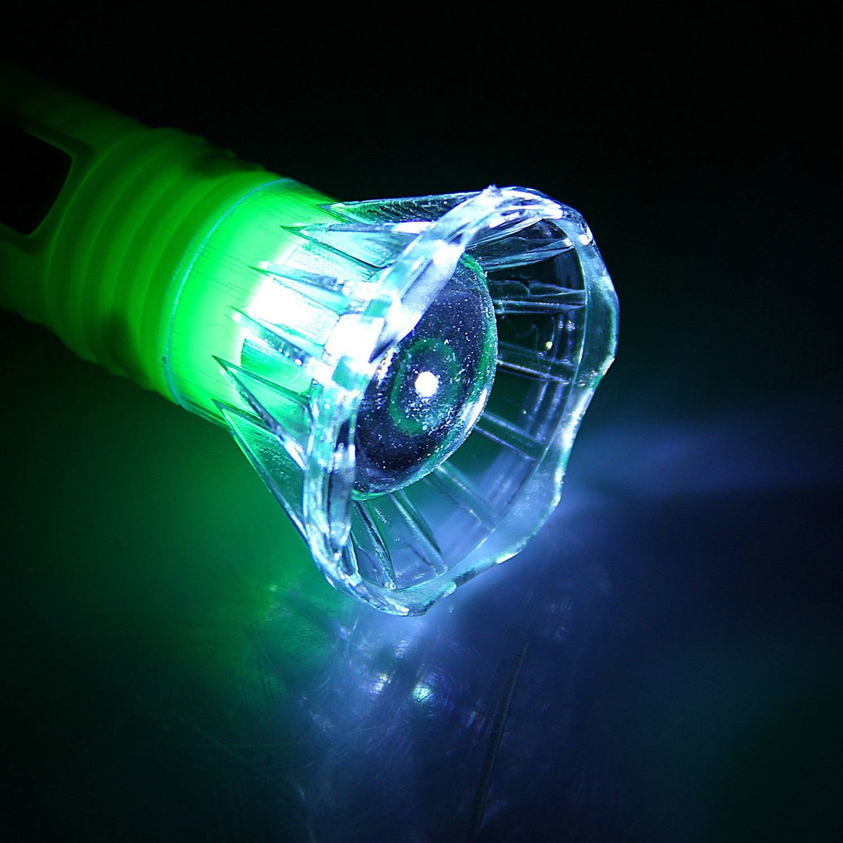 A close-up of the clear faceted head of the flashlight emitting a bright green and blue light.