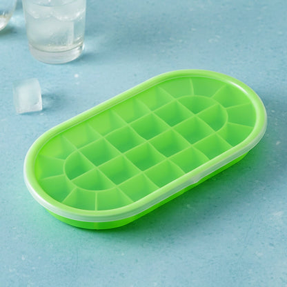 A green oval silicone ice cube tray with a clear lid, on a blue surface with a glass of ice water.