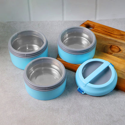 Three separate light blue lunch box containers with stainless steel interiors and a matching lid are on a cutting board.