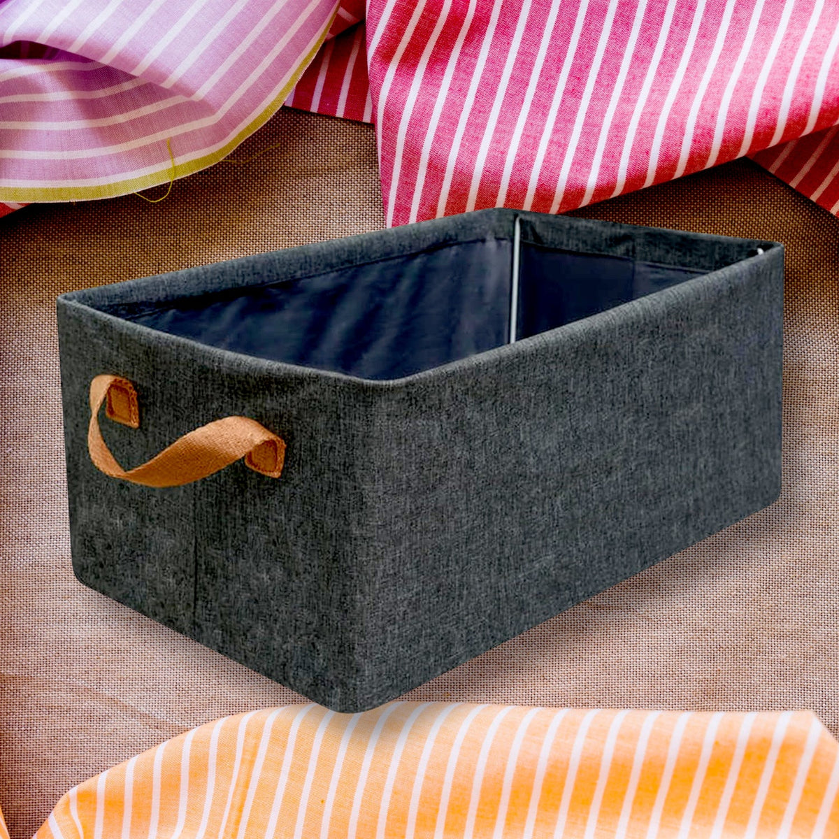 A single grey fabric storage box with brown handles on a textured surface with pink and orange striped fabric.