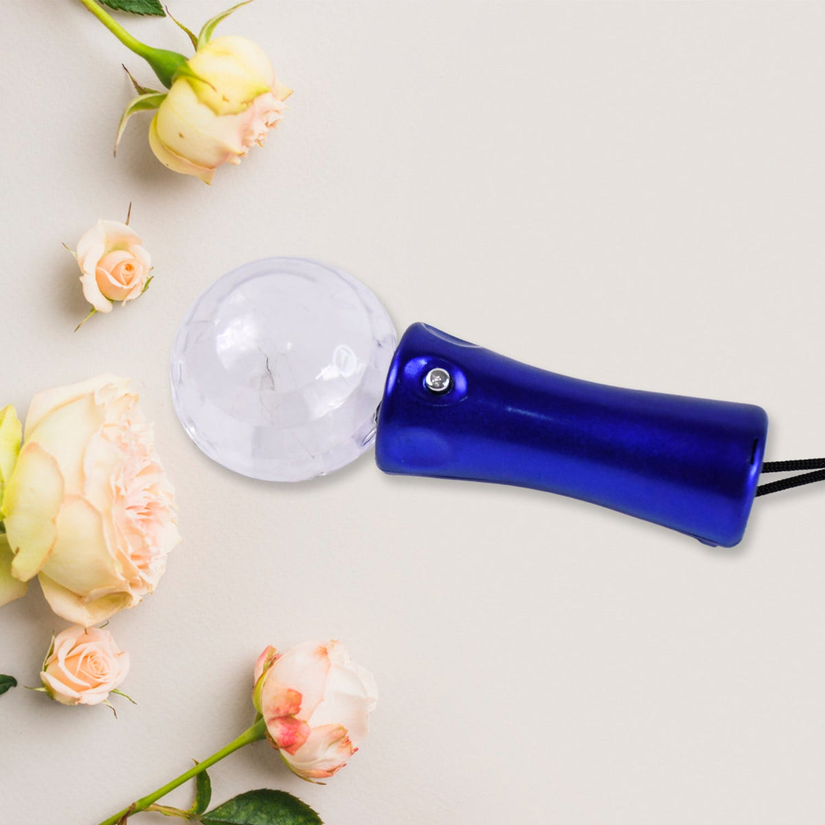Blue disco ball light wand with a black lanyard, lying horizontally on a light background with pink and cream roses.