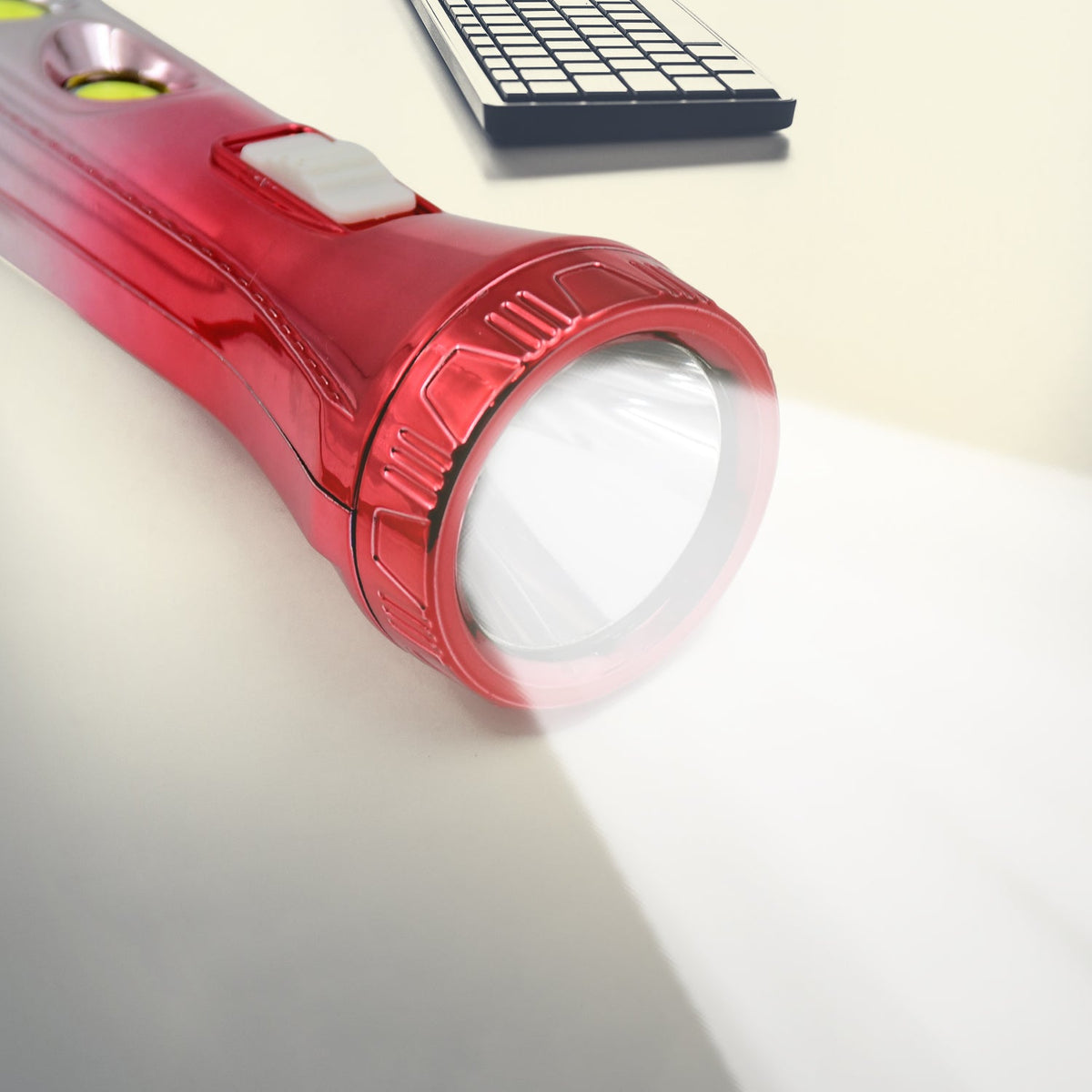 A close-up of the red and silver torchlight's head, emitting a bright light on a light surface.