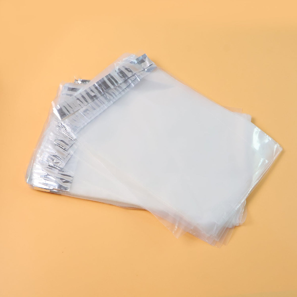 A stack of clear polybags with silver adhesive strips, angled on a light orange background.