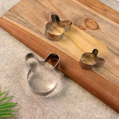 Three bunny-shaped stainless steel cookie cutters in different sizes arranged on a wooden cutting board with a green leaf